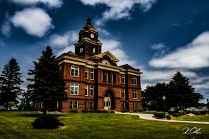 Historic red-brick courthouse with clock tower under a partly cloudy sky, surrounded by green lawn and trees