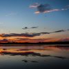 A vivid sunset reflected on a calm lake with fiery clouds and deep blue sky