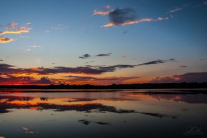 A vivid sunset reflected on a calm lake with fiery clouds and deep blue sky