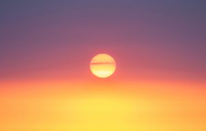 A bright sun setting with a vibrant gradient of orange to purple hues filling the sky.