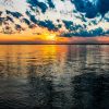 Sunset over a vast lake with vibrant orange and blue hues, scattered clouds reflecting on the water's surface.