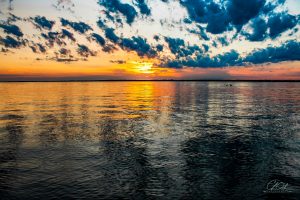 Sunset over a vast lake with vibrant orange and blue hues, scattered clouds reflecting on the water's surface.