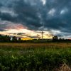 A wind turbine under a dramatic sky with a field in the foreground at sunset.