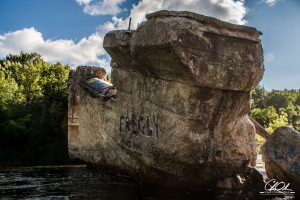Large weathered concrete structure with graffiti, surrounded by trees and under a partly cloudy sky.