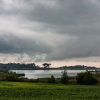 A stormy landscape with dark clouds looming over a serene lake and lush green fields.