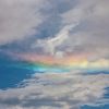 A sky with scattered clouds and a vibrant, horizontal rainbow-like spectrum.