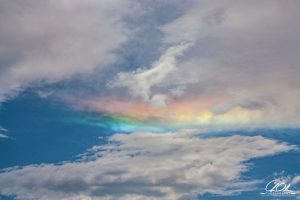 A sky with scattered clouds and a vibrant, horizontal rainbow-like spectrum.