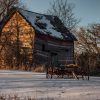 Old weathered barn with rusty farm equipment in snow-covered landscape