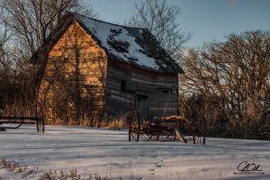 Old weathered barn with rusty farm equipment in snow-covered landscape