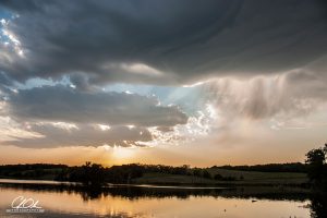 A serene sunset over a peaceful lake with clouds gathering in the sky.