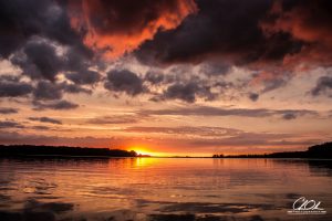 A dramatic sunset over a calm lake with vibrant orange and purple clouds.