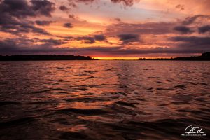 Vibrant sunset over rippling water with dark clouds above.