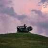An old, rusted machine sits atop a gentle grassy hill under a dramatic, colorful sky at dusk.