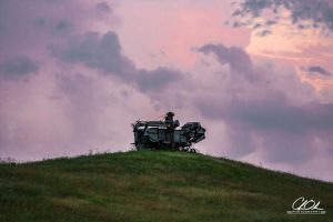 An old, rusted machine sits atop a gentle grassy hill under a dramatic, colorful sky at dusk.