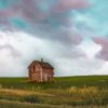An old wooden farmhouse stands alone in a vast green field beneath a picturesque sky with colorful, swirling clouds.