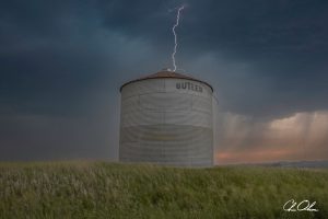 Grain bin with lightning strike in open field under dark stormy sky.