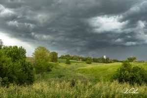 A landscape with dark storm clouds looming over lush green fields and scattered trees