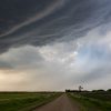 Dirt road stretching under dramatic storm clouds in a rural landscape.