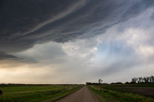 Dirt road stretching under dramatic storm clouds in a rural landscape.