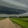 Gravel road leading towards a distant farm under a dark, looming storm cloud.