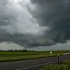 Dark storm clouds looming over an open road and green fields.