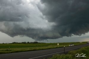 Dark storm clouds looming over an open road and green fields.