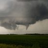 Dark storm clouds with a visible funnel over a green field