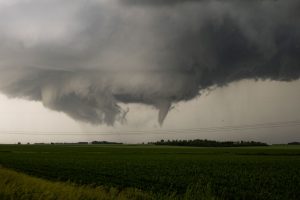 Dark storm clouds with a visible funnel over a green field