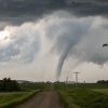 A tornado touching down in a rural area with power lines and a dirt road.