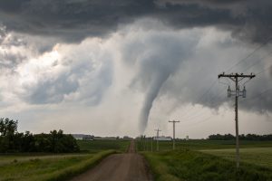 A tornado touching down in a rural area with power lines and a dirt road.