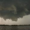 Large dark storm clouds above a body of water with a distant horizon of trees.