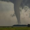 A large tornado funnel cloud above a flat landscape with trees and fields.